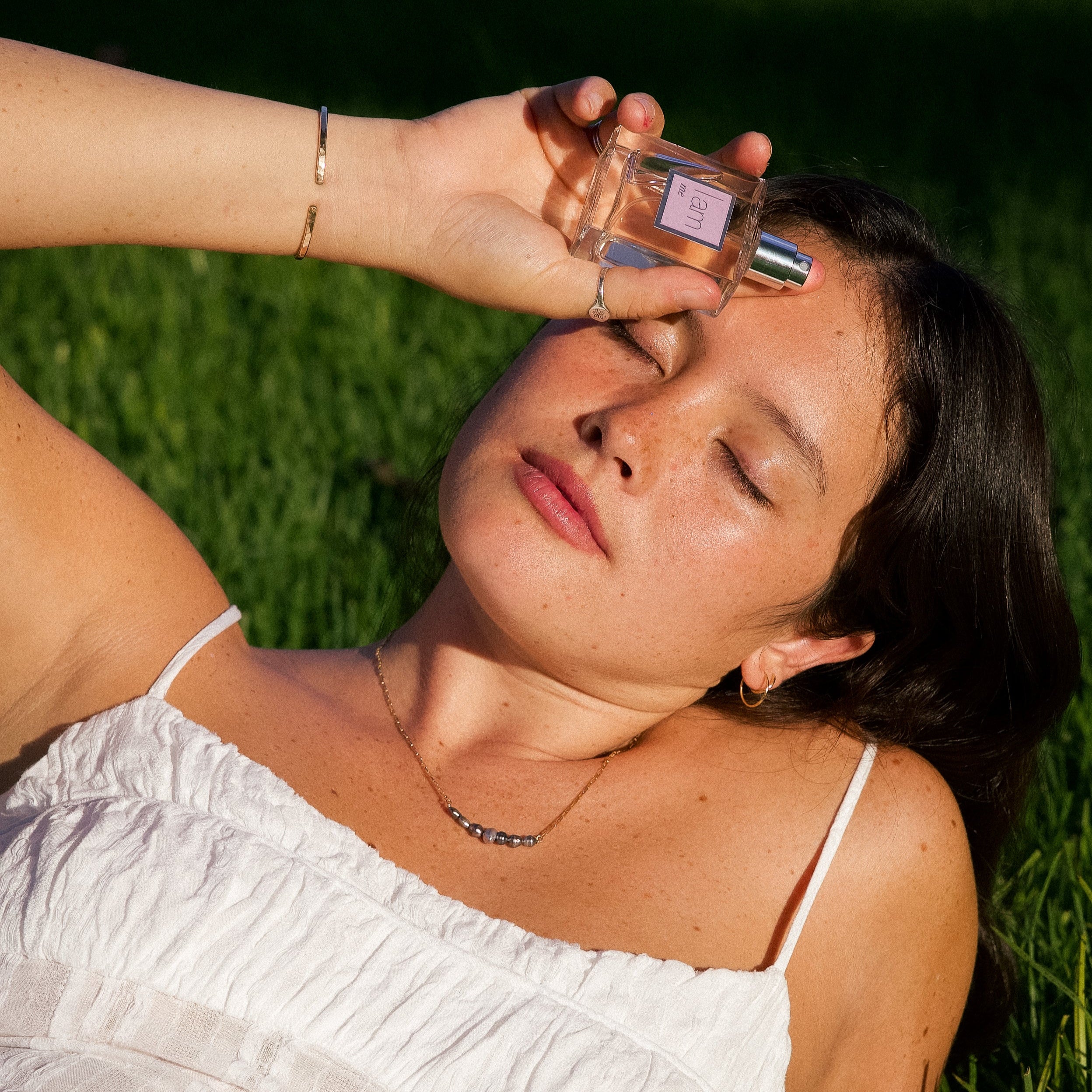 Woman applying perfume outdoors on a grassy background