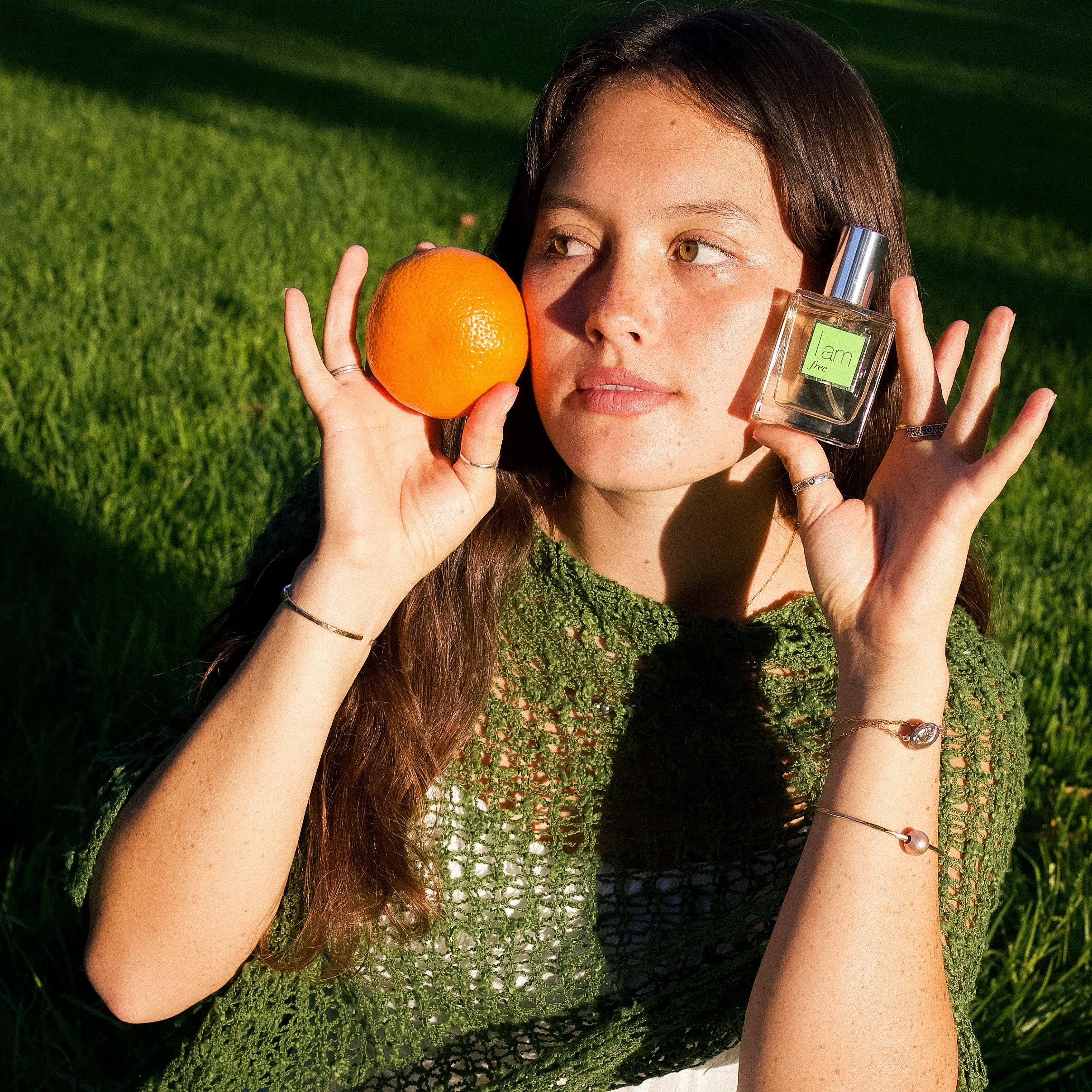 Woman holding an orange and a perfume bottle outdoors on grass