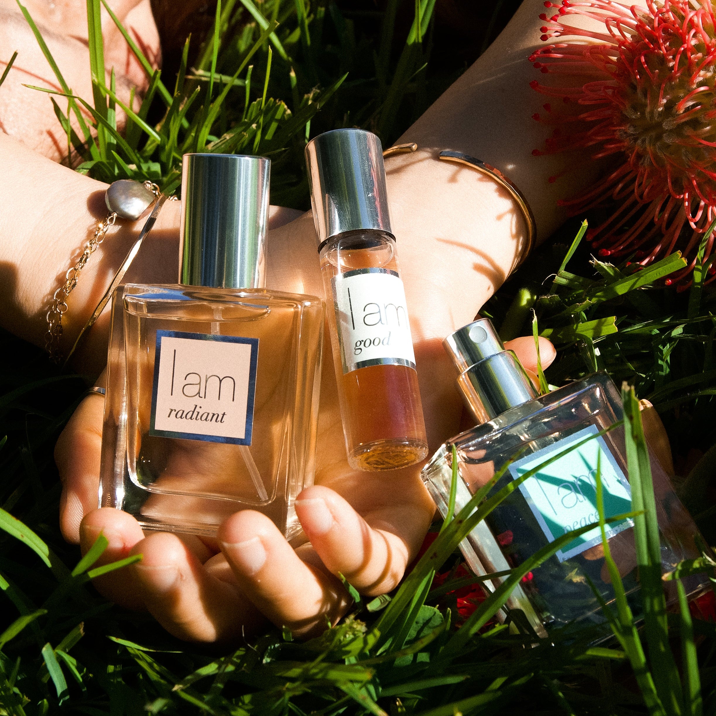 Three perfume bottles held in hands with grass and flowers in the background
