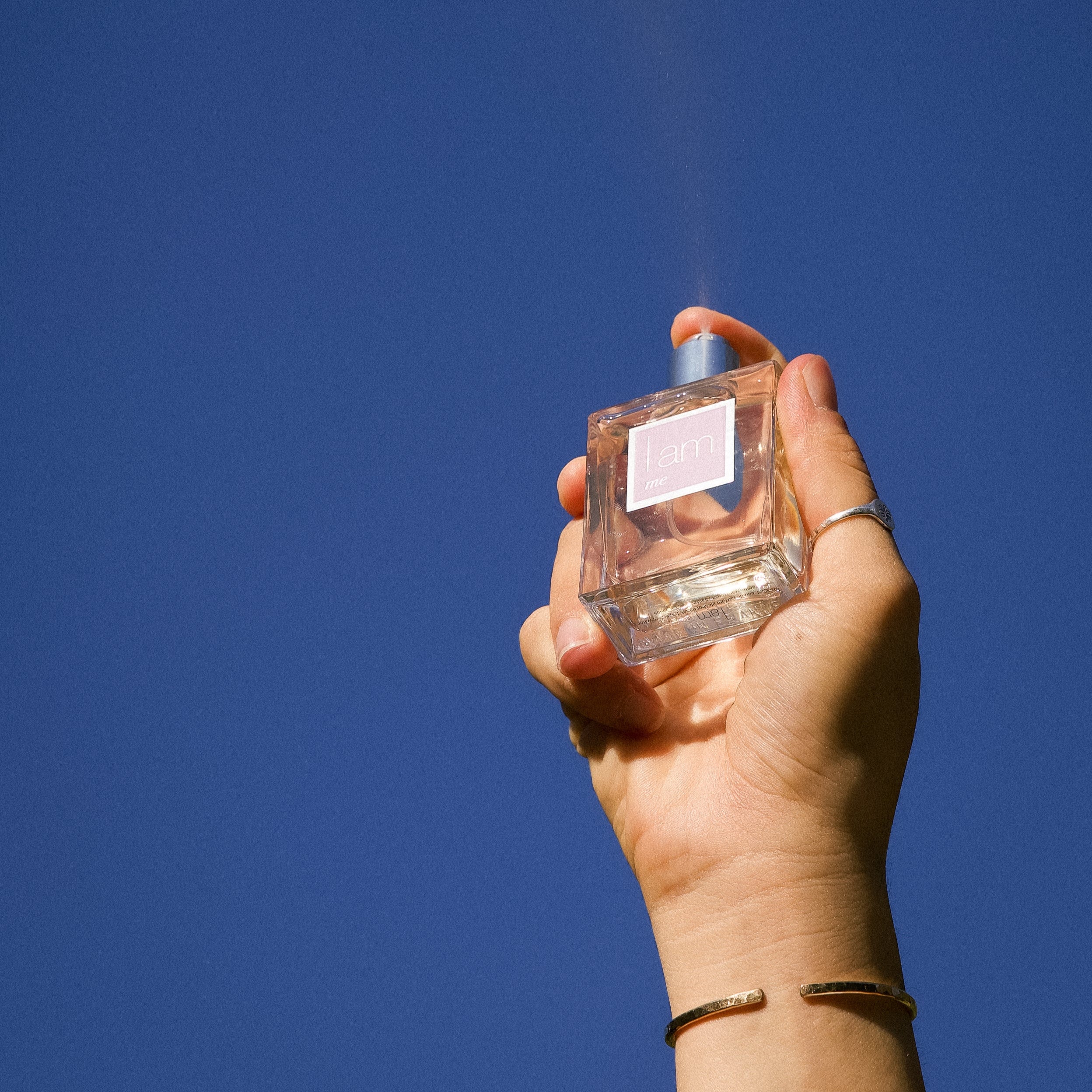 Hand holding a perfume bottle against a clear blue sky