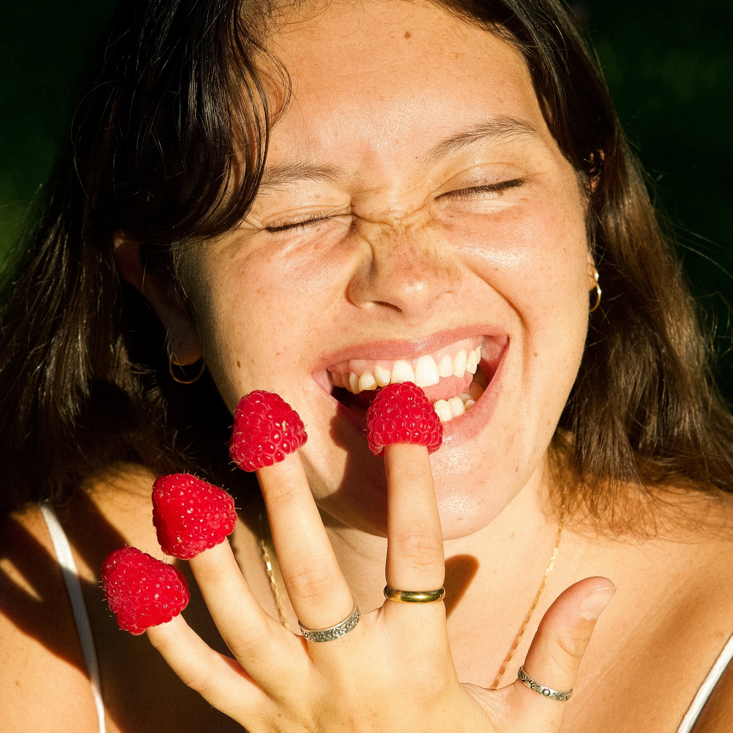 Woman with raspberries on her fingers and in her mouth, outdoors.