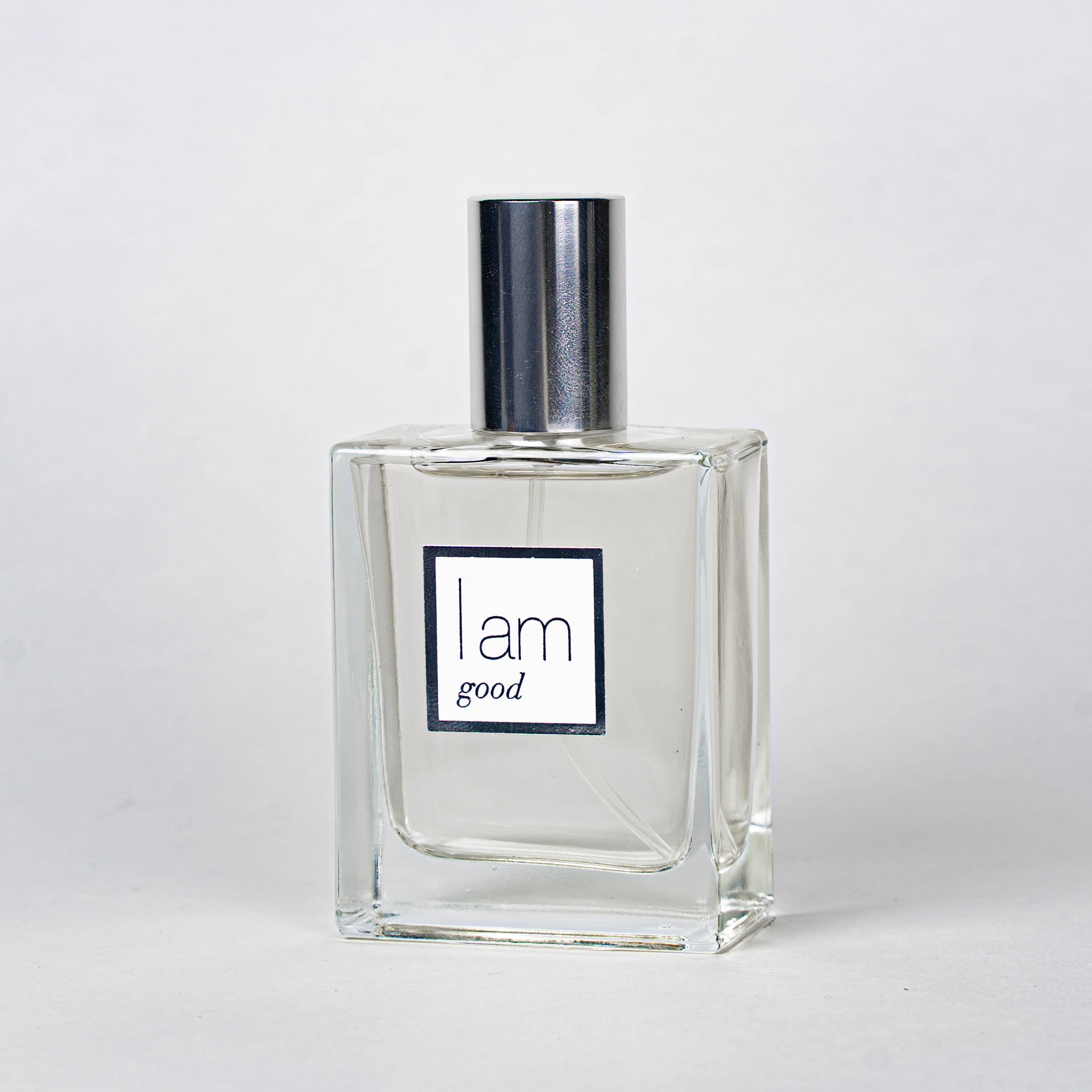 Clear perfume bottle with silver cap and 'I am good' label on a white background