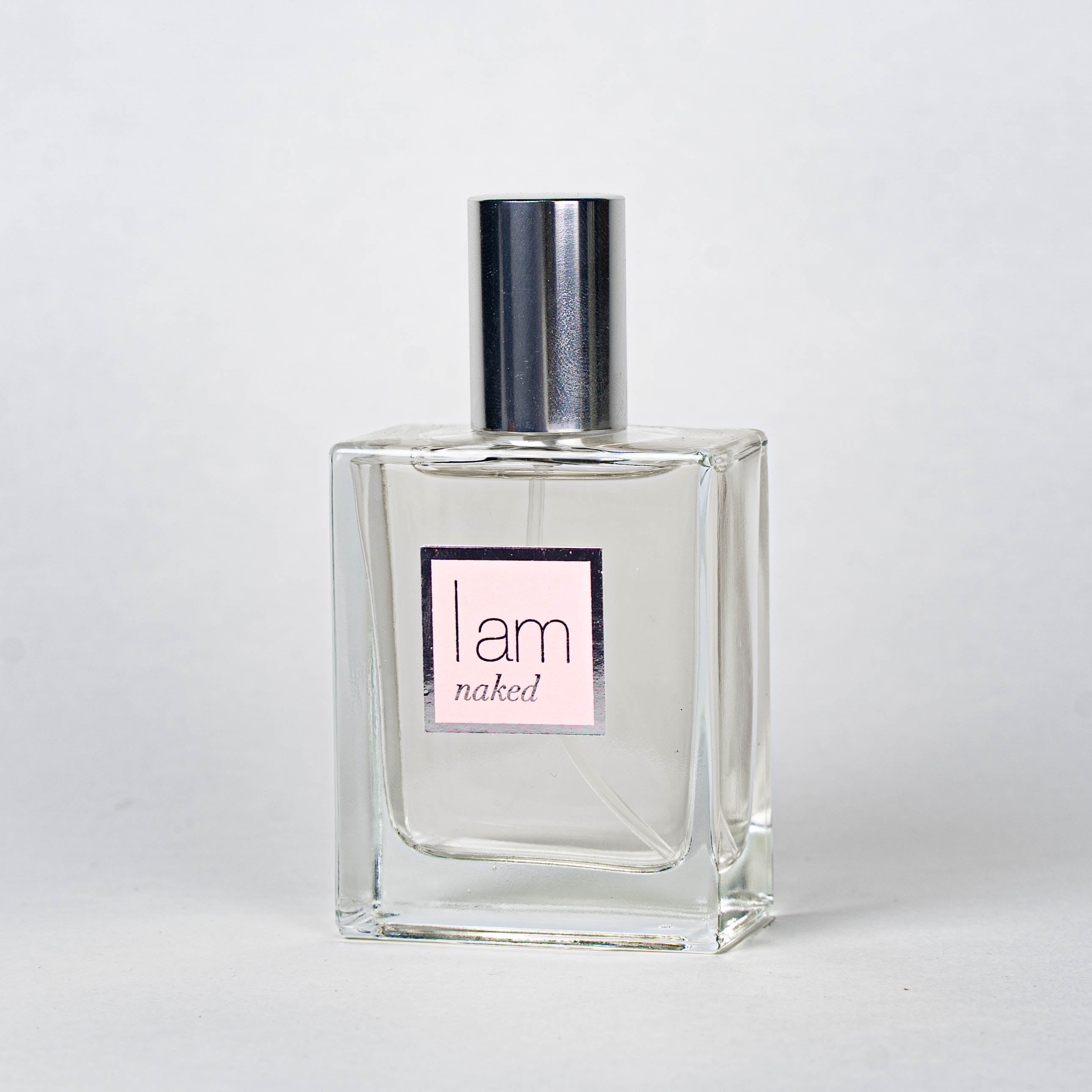 Clear perfume bottle with silver cap and 'I am naked' label on a white background