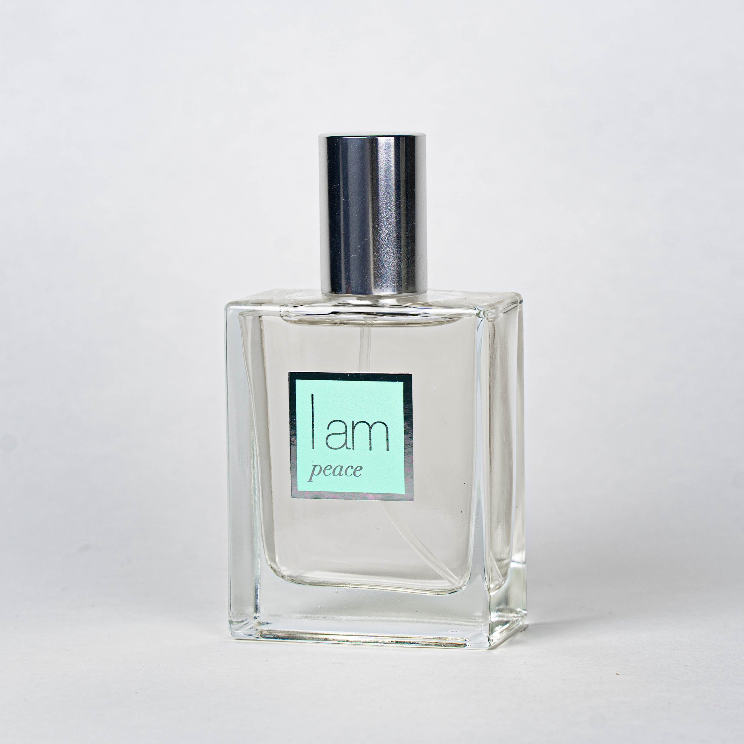 Clear perfume bottle with a silver cap and 'I am peace' label on a white background