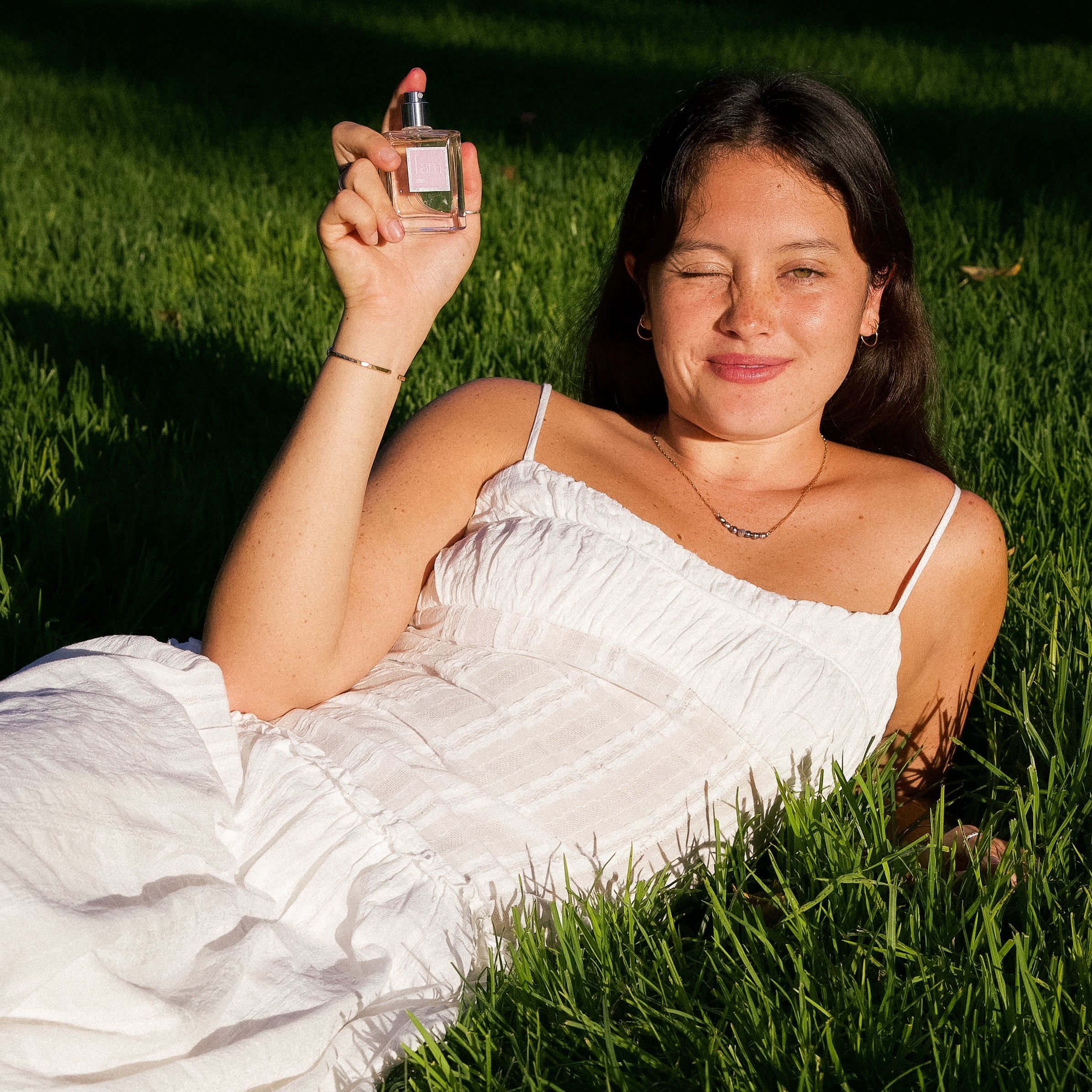 Woman in a white dress holding perfume in grass